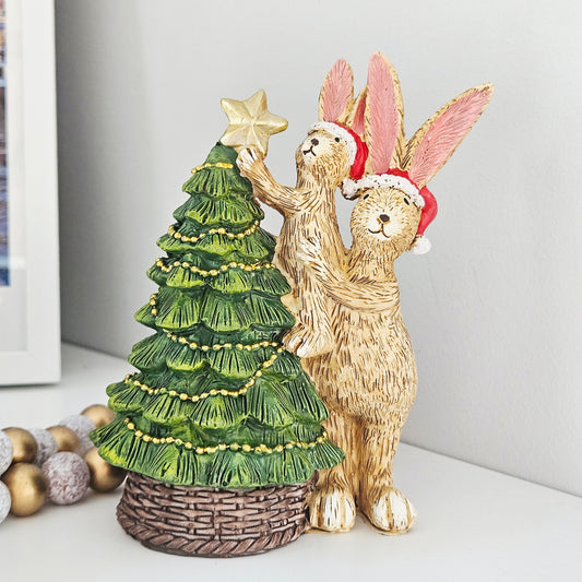 Decorative figurine of two jasper rabbits with a Christmas tree putting star on the top wearing santa hats