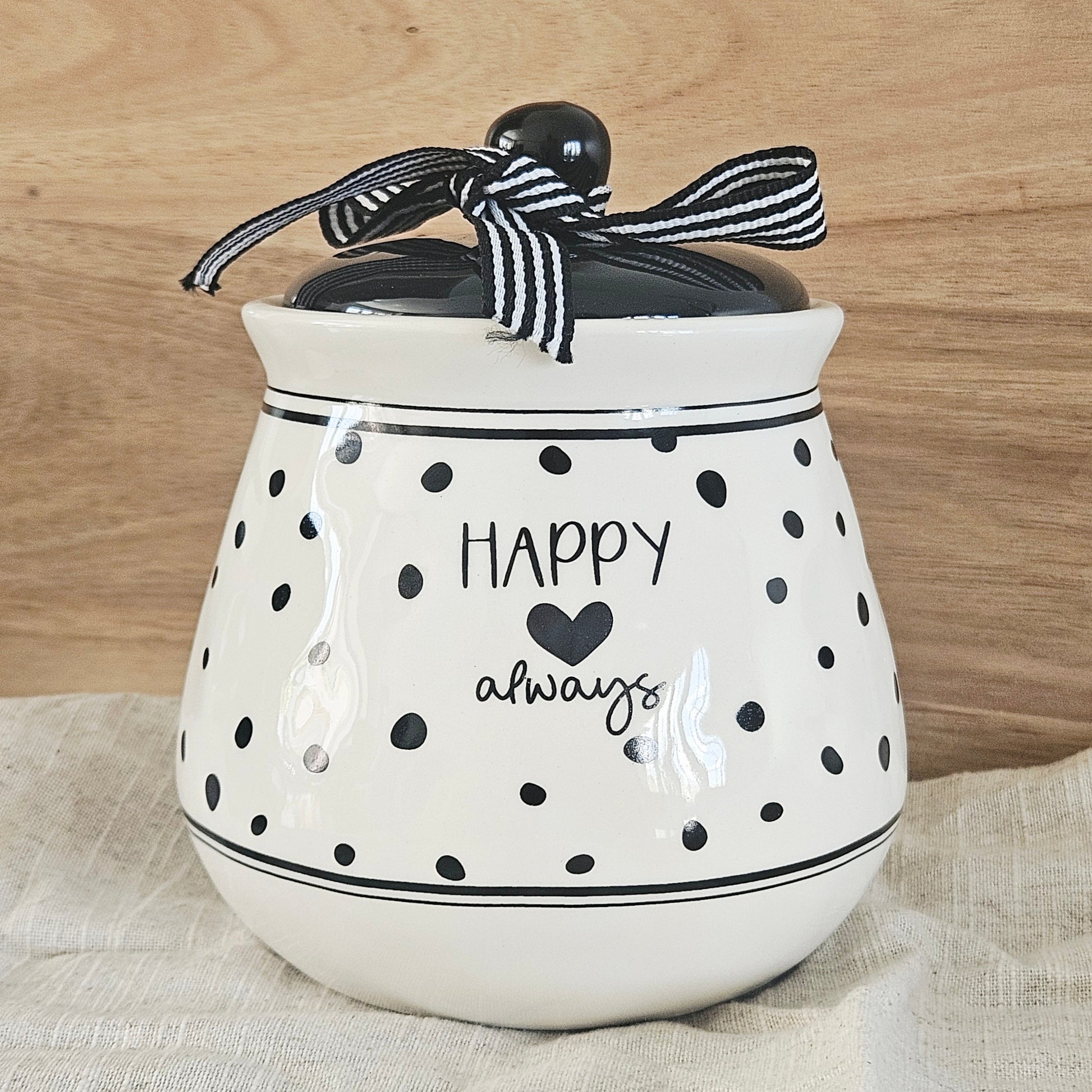 White ceramic jar with black polka dots and text, tied with a black and white striped ribbon, happy always text