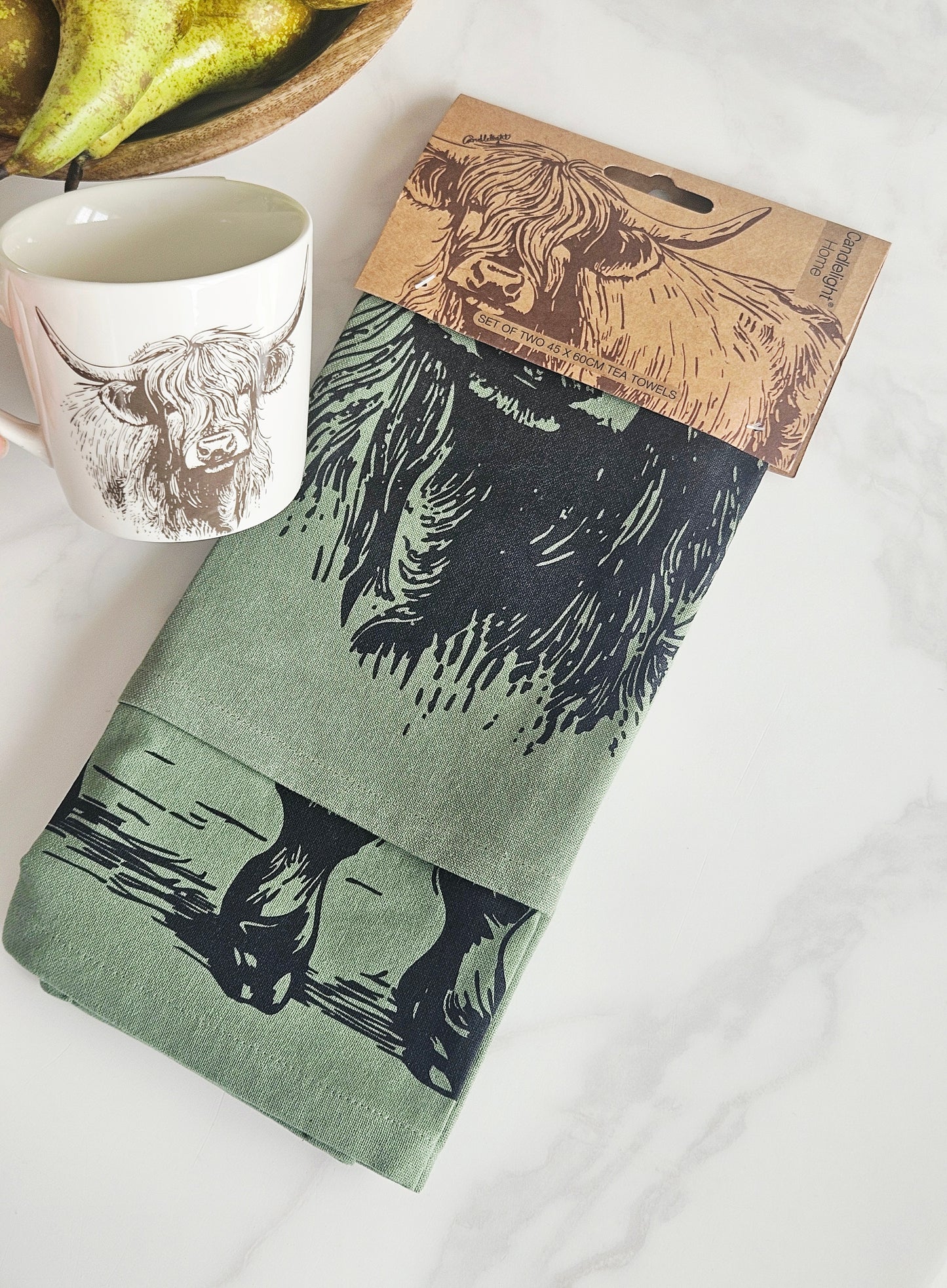 2 Green tea towels with a printed design of a highland cow displayed with a cardboard holder 