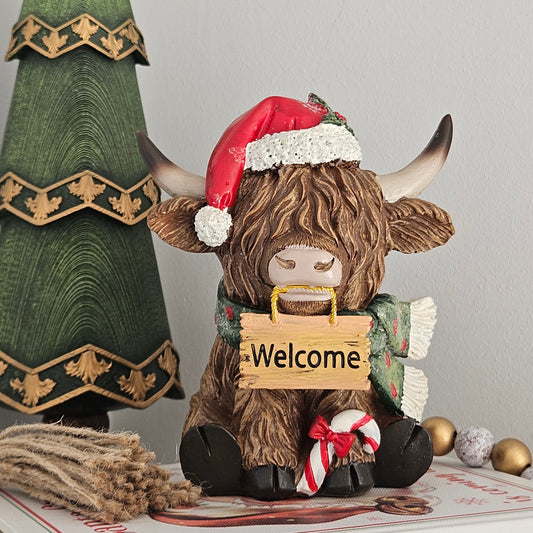 decorative figure highland cow with red santa hat holding a welcome sign in it's mouth