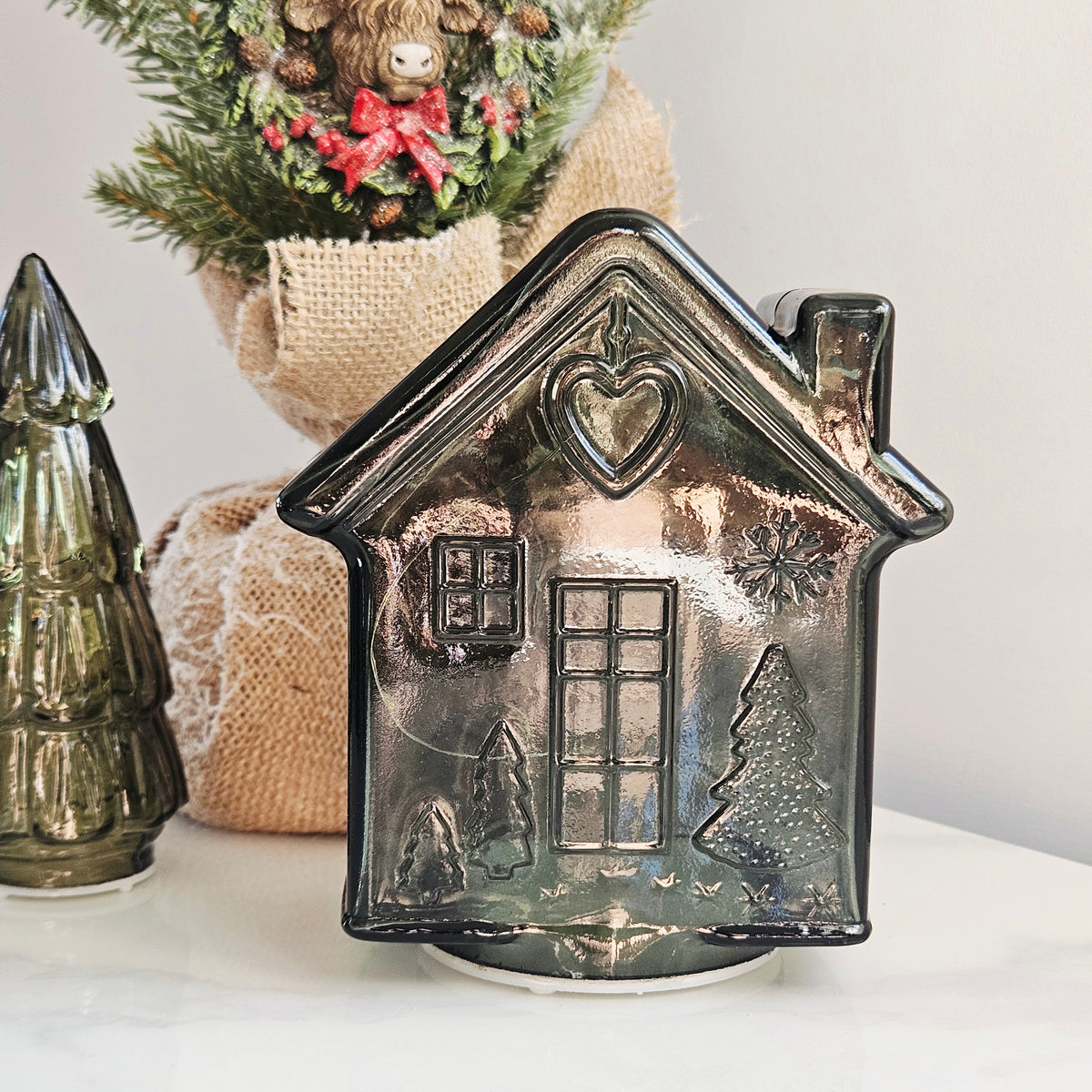 A glossy glass gingerbread led house-shaped ornament with embossed holiday details like a window, door, Christmas tree, and snowflake