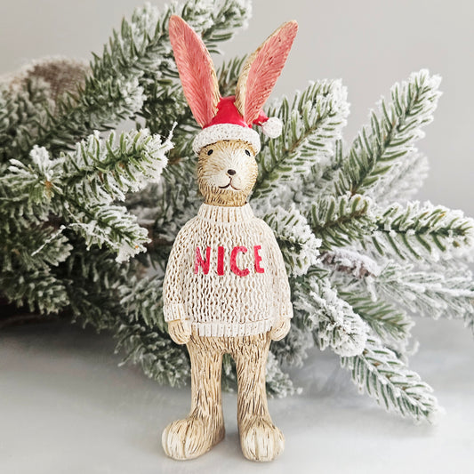 A decorative rabbit figurine wearing a red Santa hat and a cream knit sweater with the word 'NICE' in red,