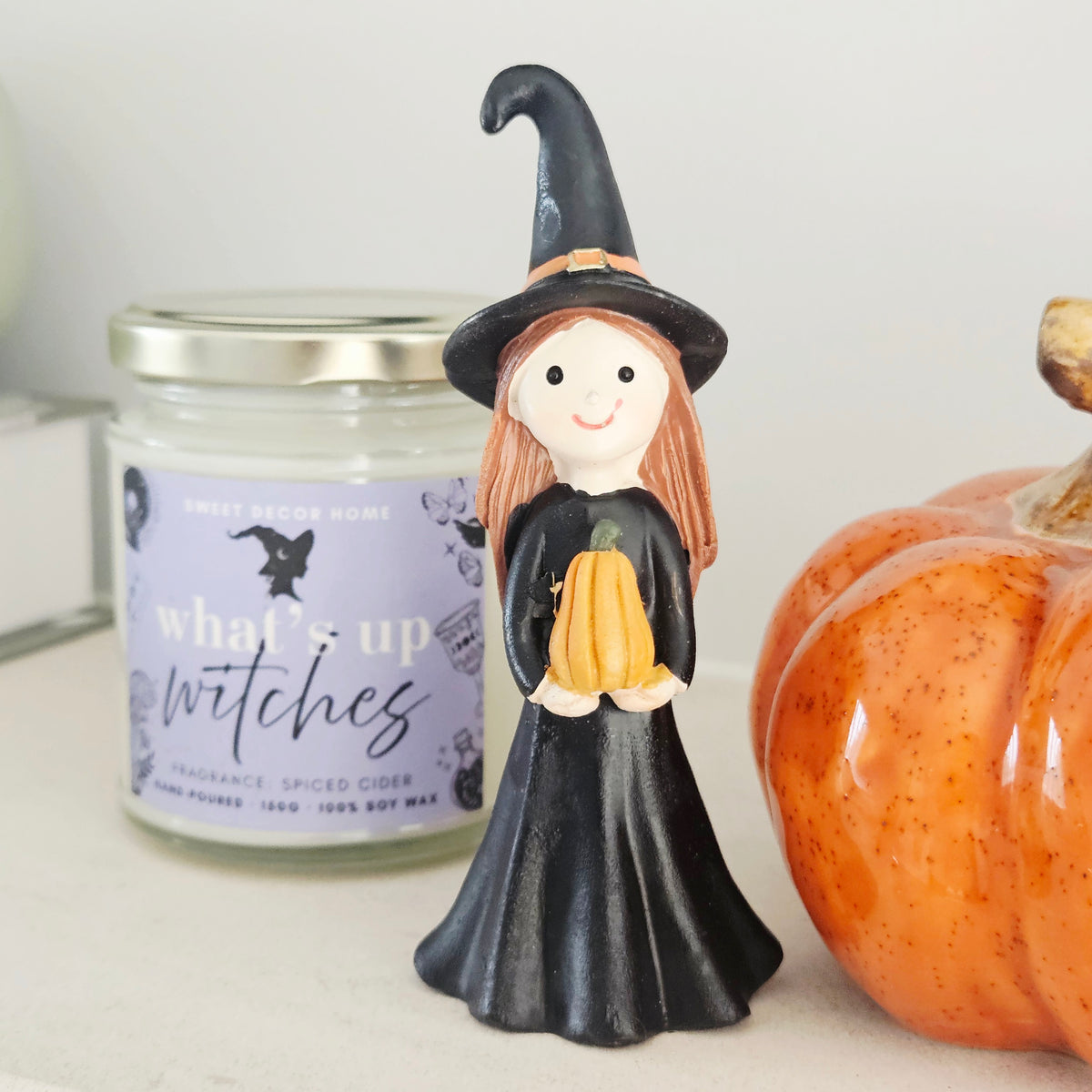 A hand-painted ceramic witch figurine holding a small orange pumpkin, 
