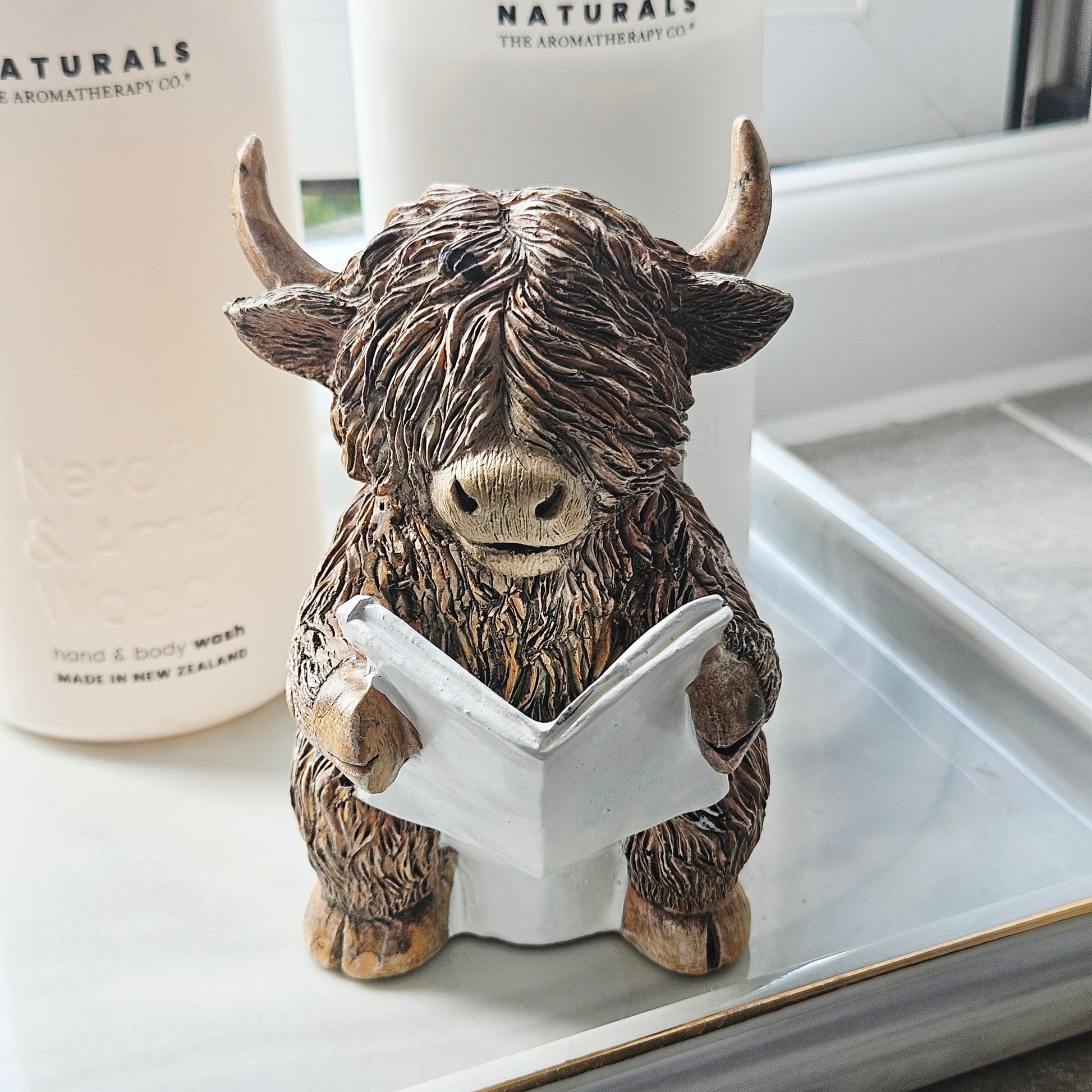 Statue of a Highland cow reading a book sitting on a toilet