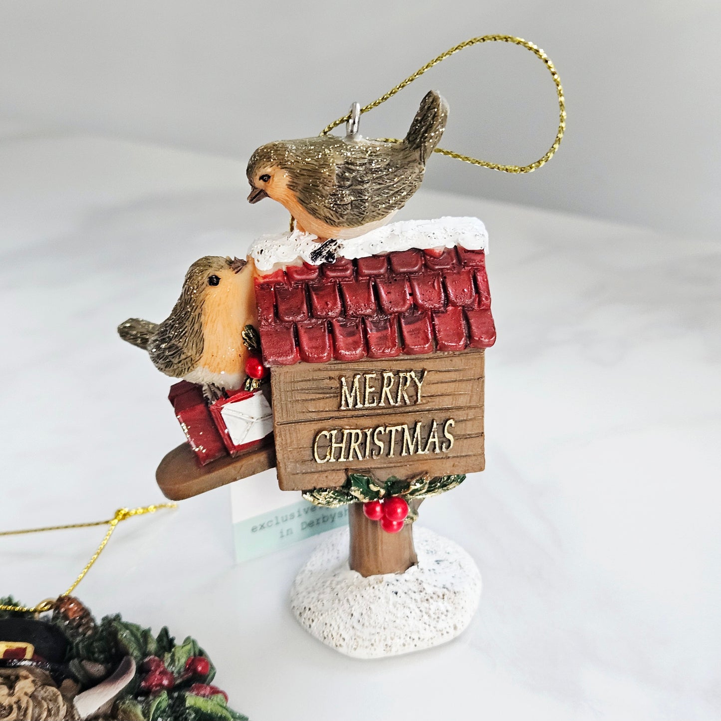 Christmas ornament with two birds on a roof sign saying 'Merry Christmas' on a white background