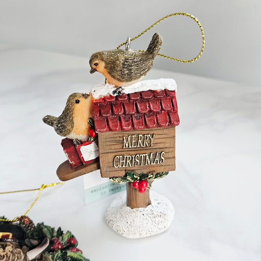 Christmas ornament with two birds on a roof sign saying 'Merry Christmas' on a white background