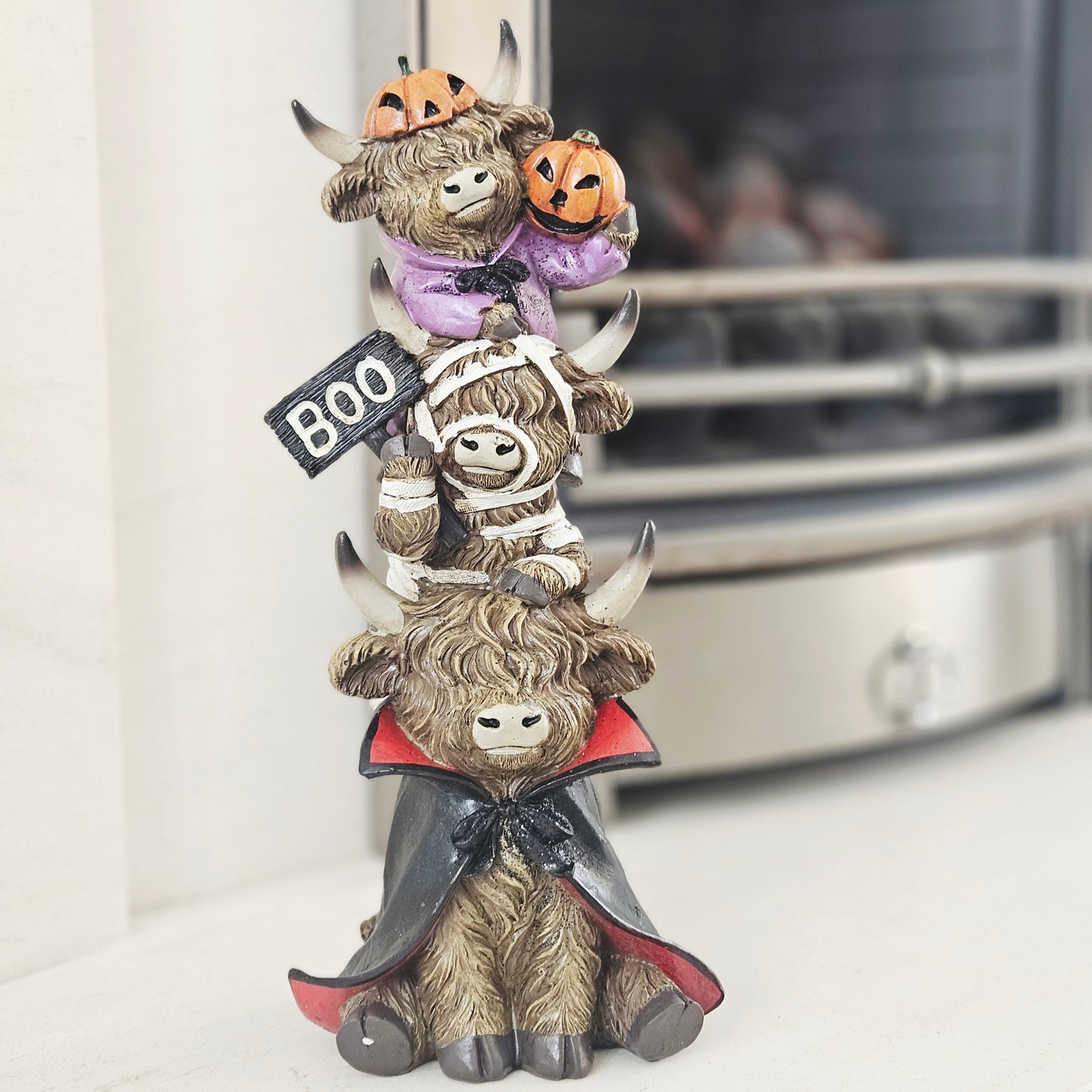 A stacked Halloween figurine of three cartoonish buffalos wearing costumes, with the top one holding jack-o'-lanterns and a black sign that says BOO, 