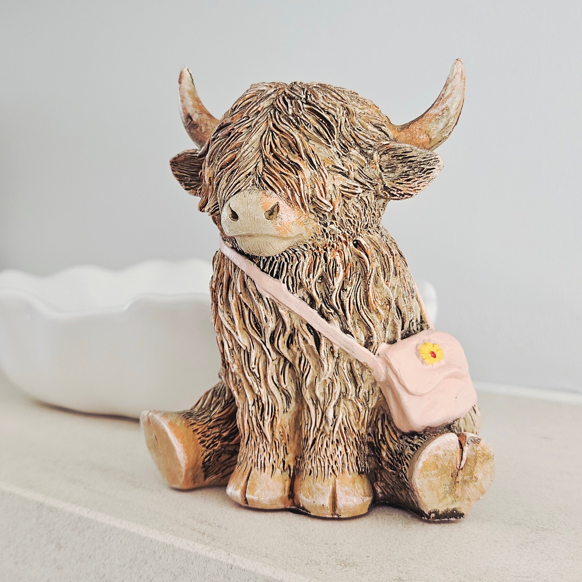 highland cow ornament wearing a pink handbag with yellow flower