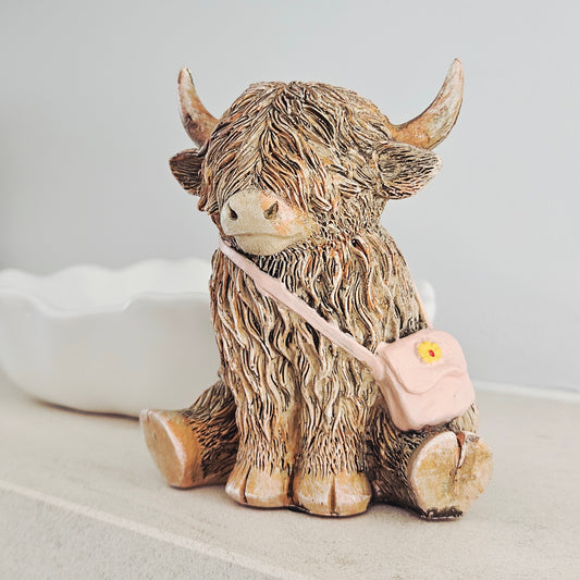 highland cow ornament wearing a pink handbag with yellow flower