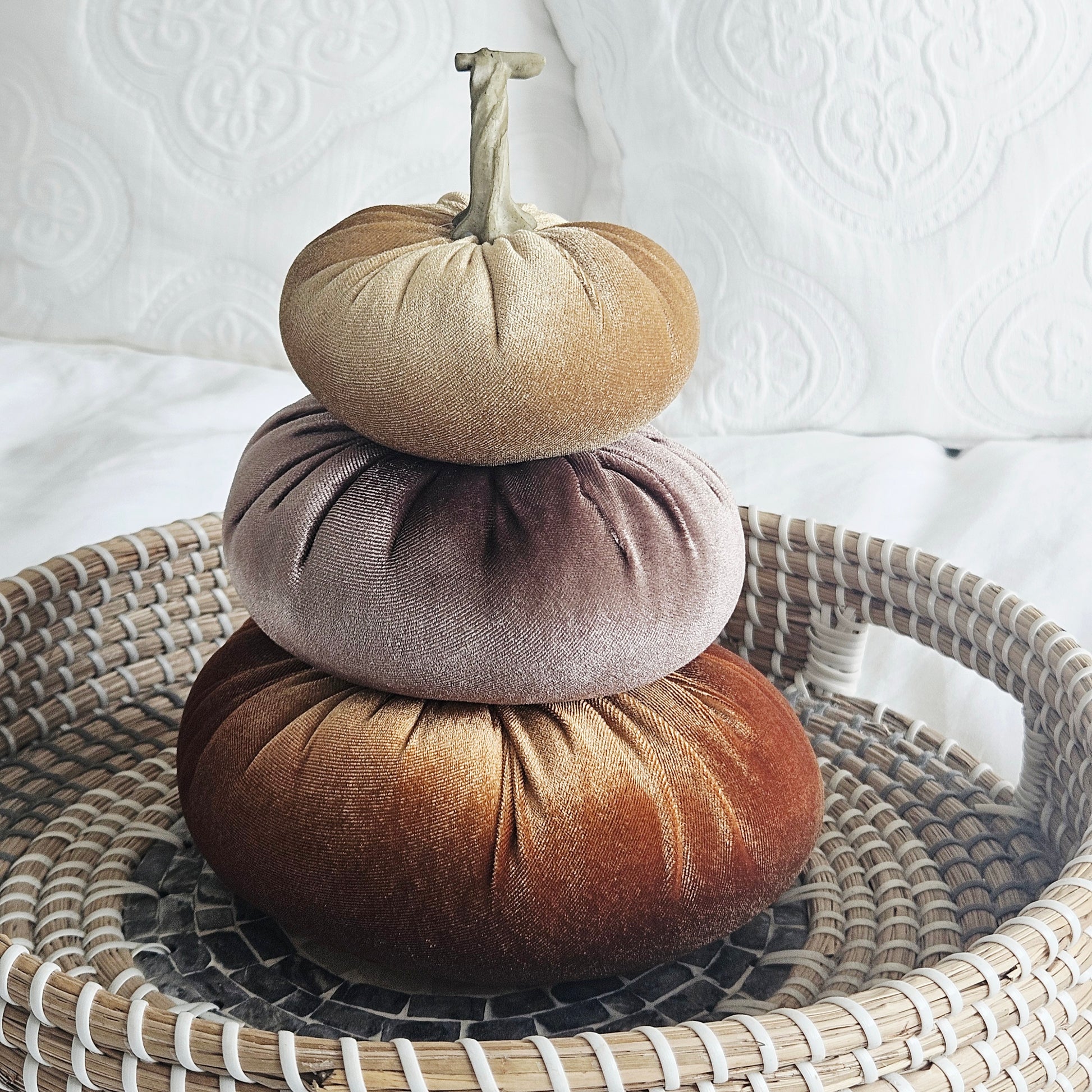 Three round velvet decorative pumpkins stacked on top of each other. The pumpkins are in shades of tan, dusty mauve, and rich brown, with a small faux stem on the top pumpkin.