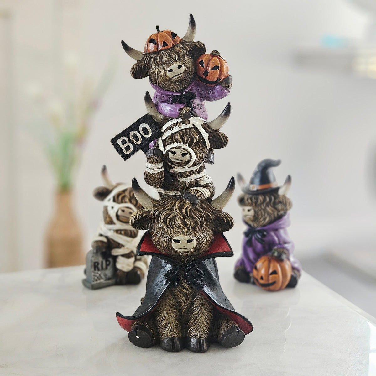 A stacked Halloween figurine of three cartoonish buffalos wearing costumes, with the top one holding jack-o'-lanterns and a black sign that says BOO, 