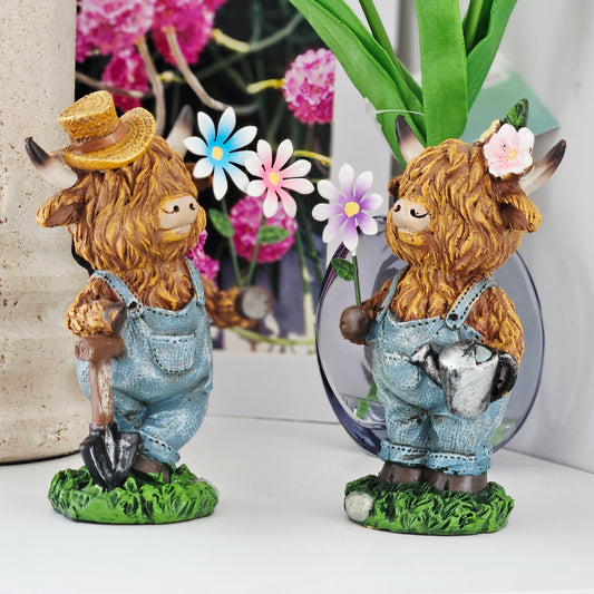 Two decorative figurines of Highland cows with hats and overalls holding flowers
