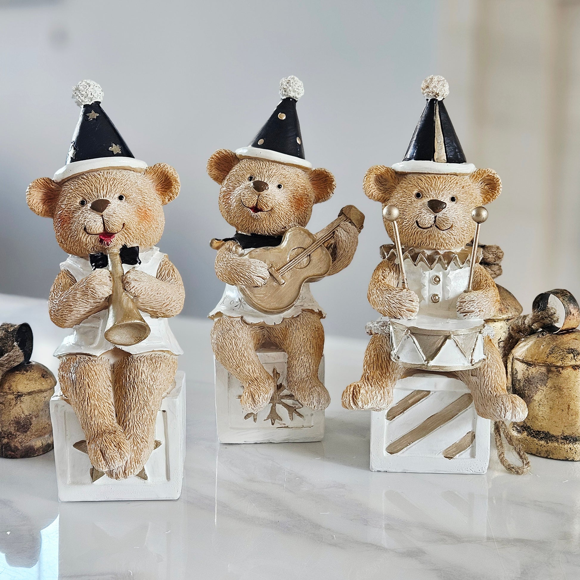 Three teddy bear figurines dressed as musicians sitting on small white stools, with one playing a trumpet, one playing a guitar, and one playing a drum