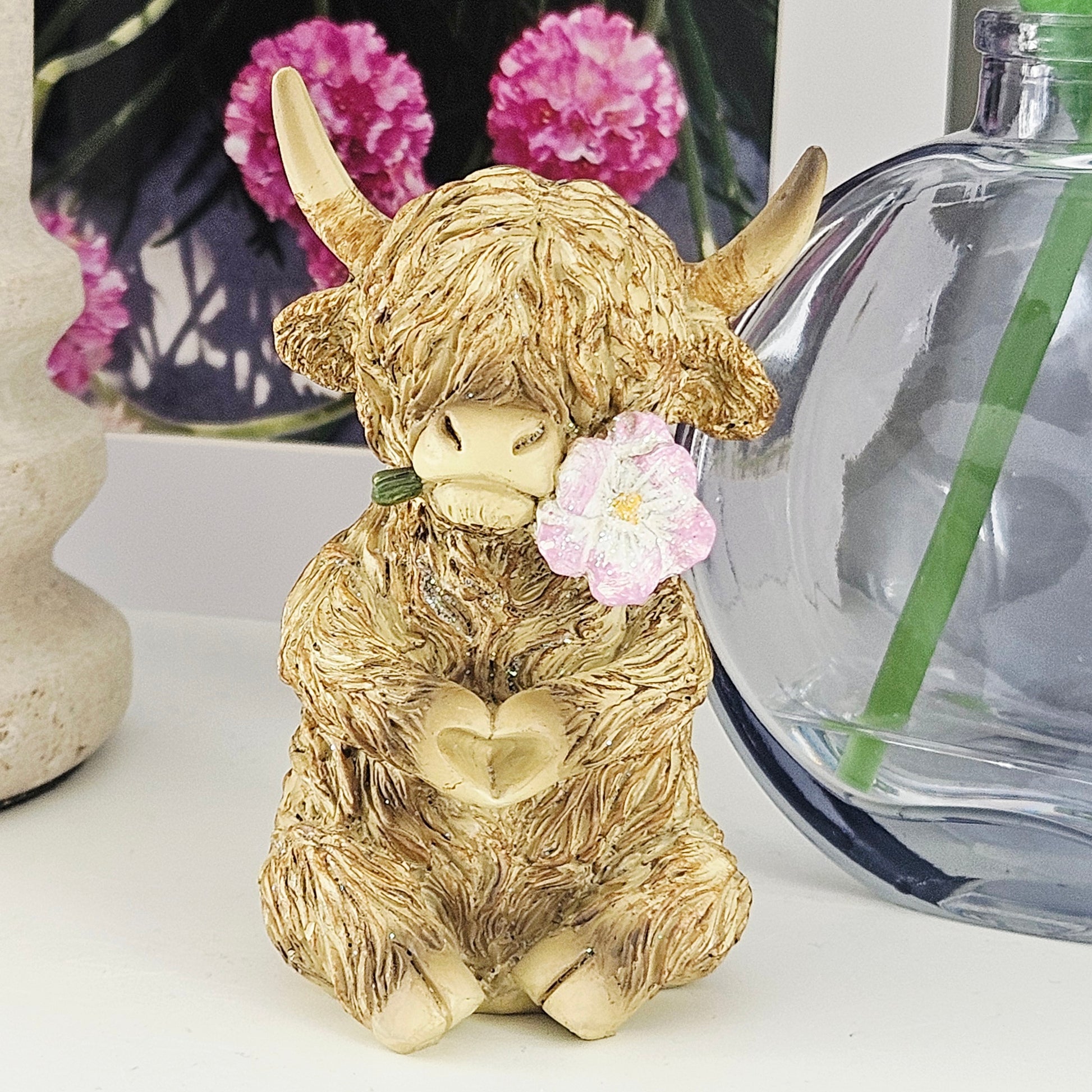Statue of a highland cow with a flowering its mouth making a heart shape with paws
