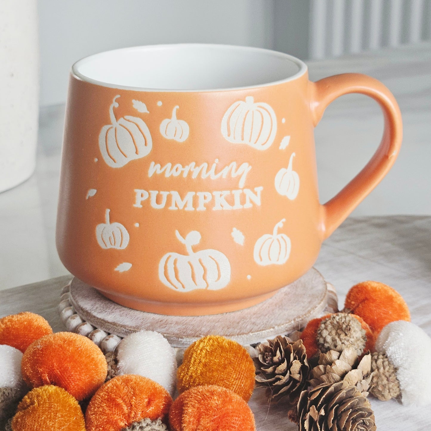 An orange ceramic mug with white pumpkin illustrations and the words 'morning PUMPKIN' on the front, 
