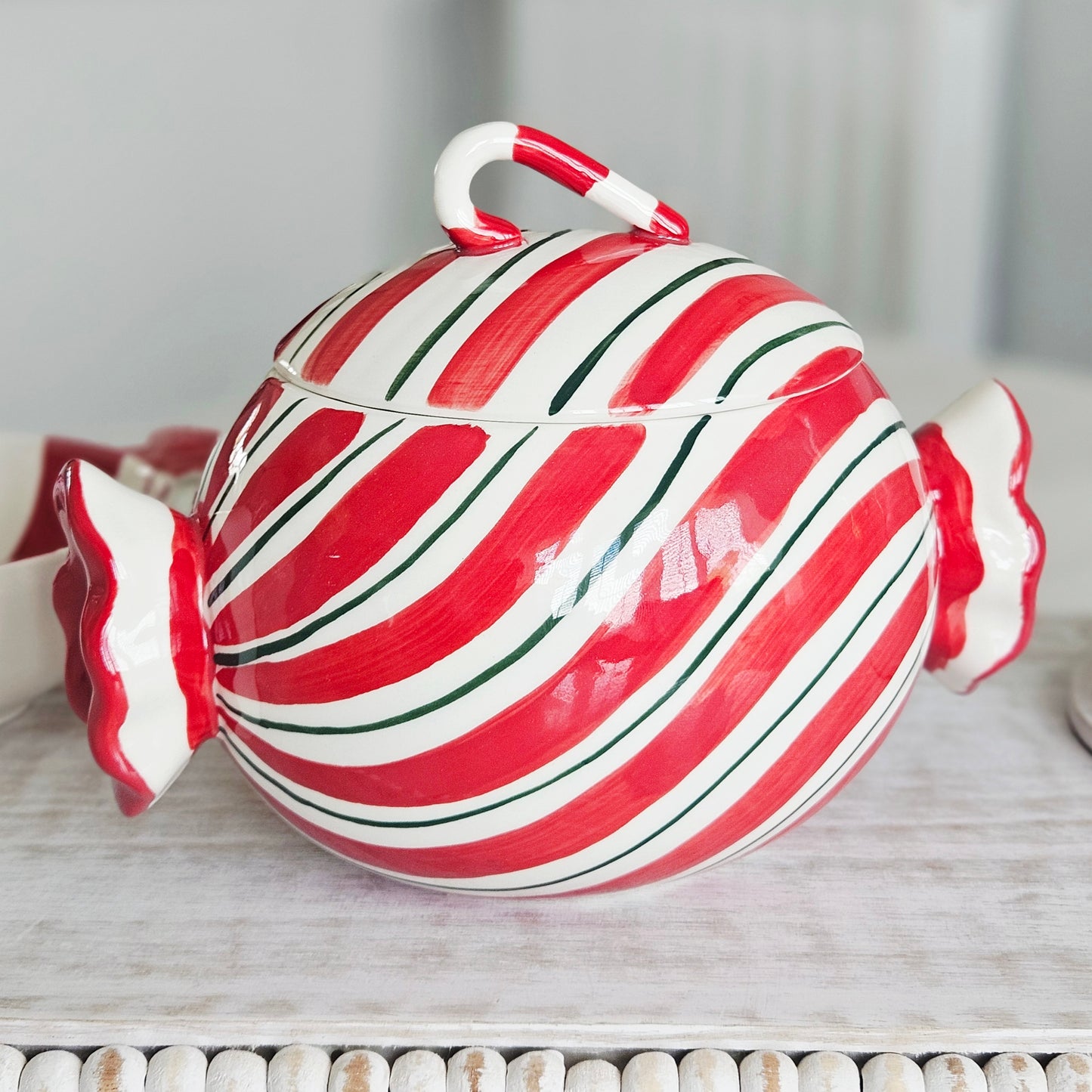 A glossy ceramic candy- sweet shaped lidded storage jar ceramic with red and white diagonal stripes, green accent lines, and a candy cane handle on top