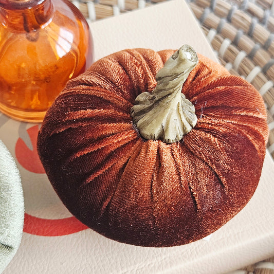 A small velvet decorative pumpkin in a warm rust-orange colour with a textured faux-stem, 