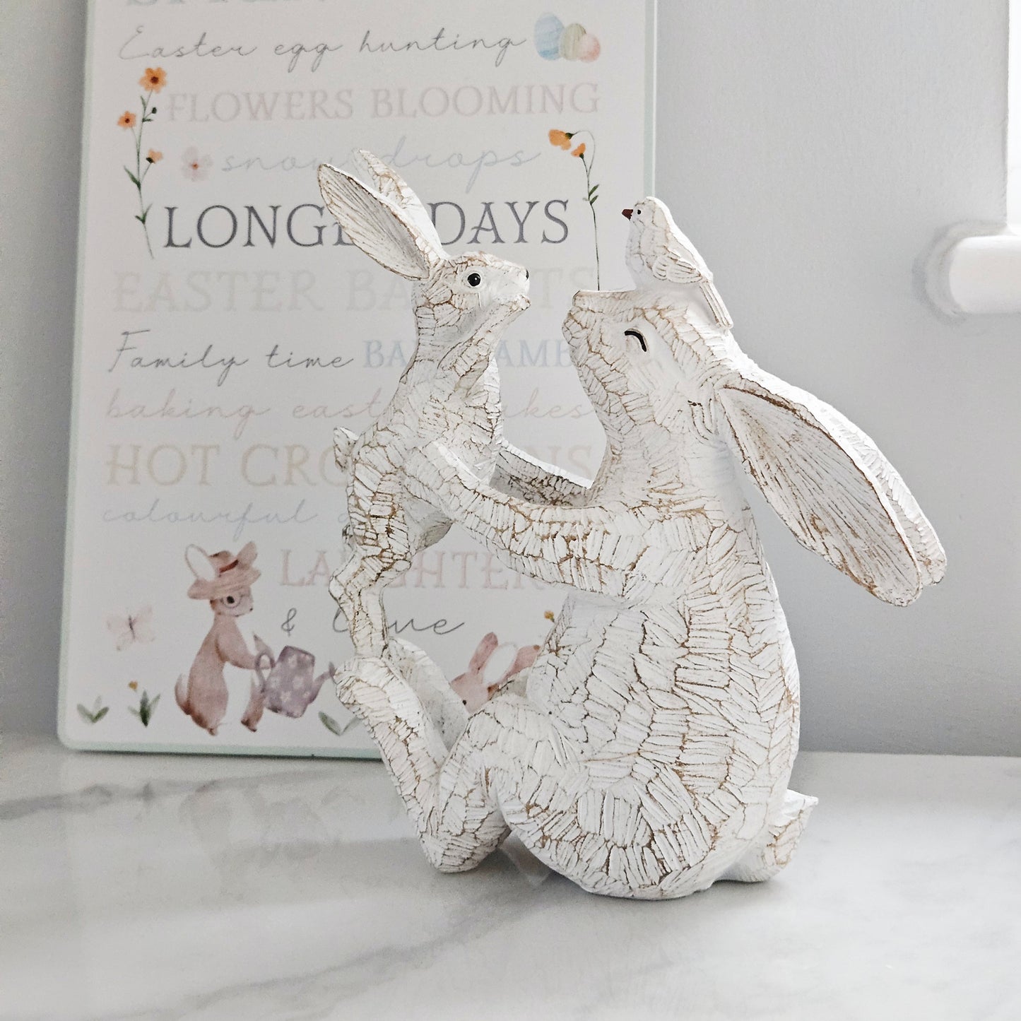 Decorative white rabbit figurine holding a baby rabbit and bird on mums head
