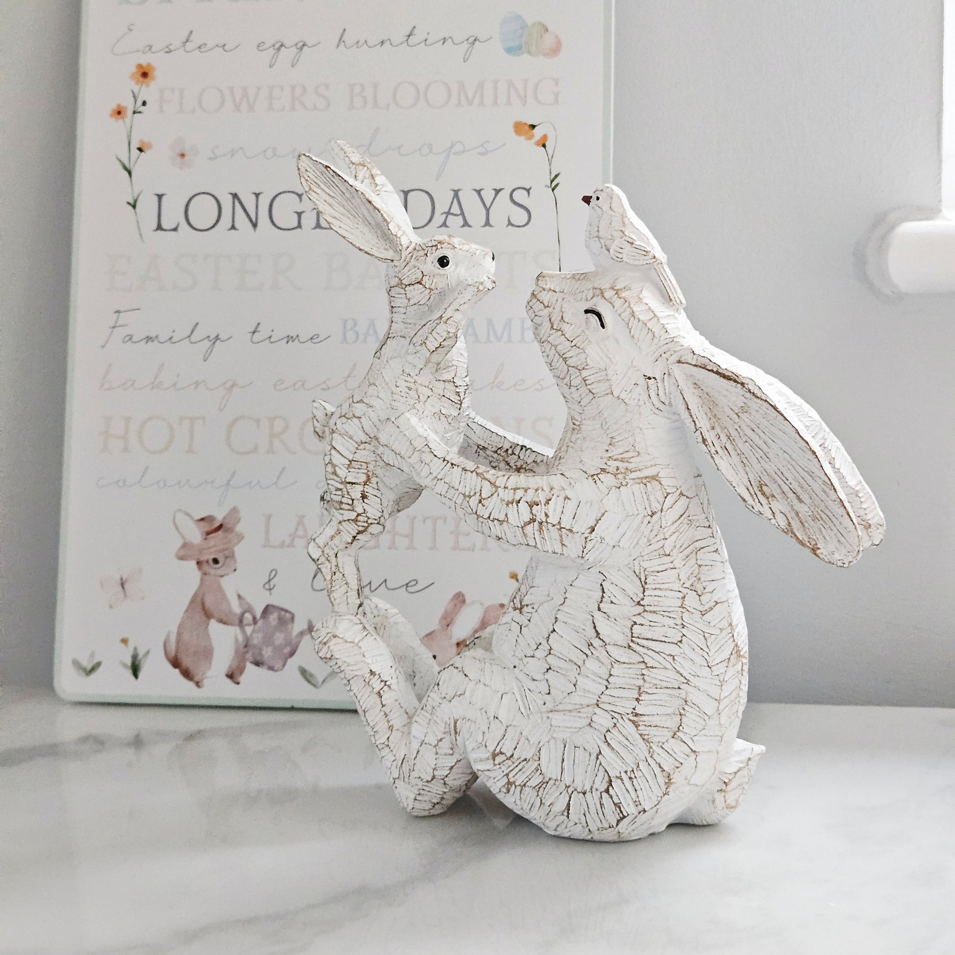 Decorative white rabbit figurine holding a baby rabbit and bird on mums head