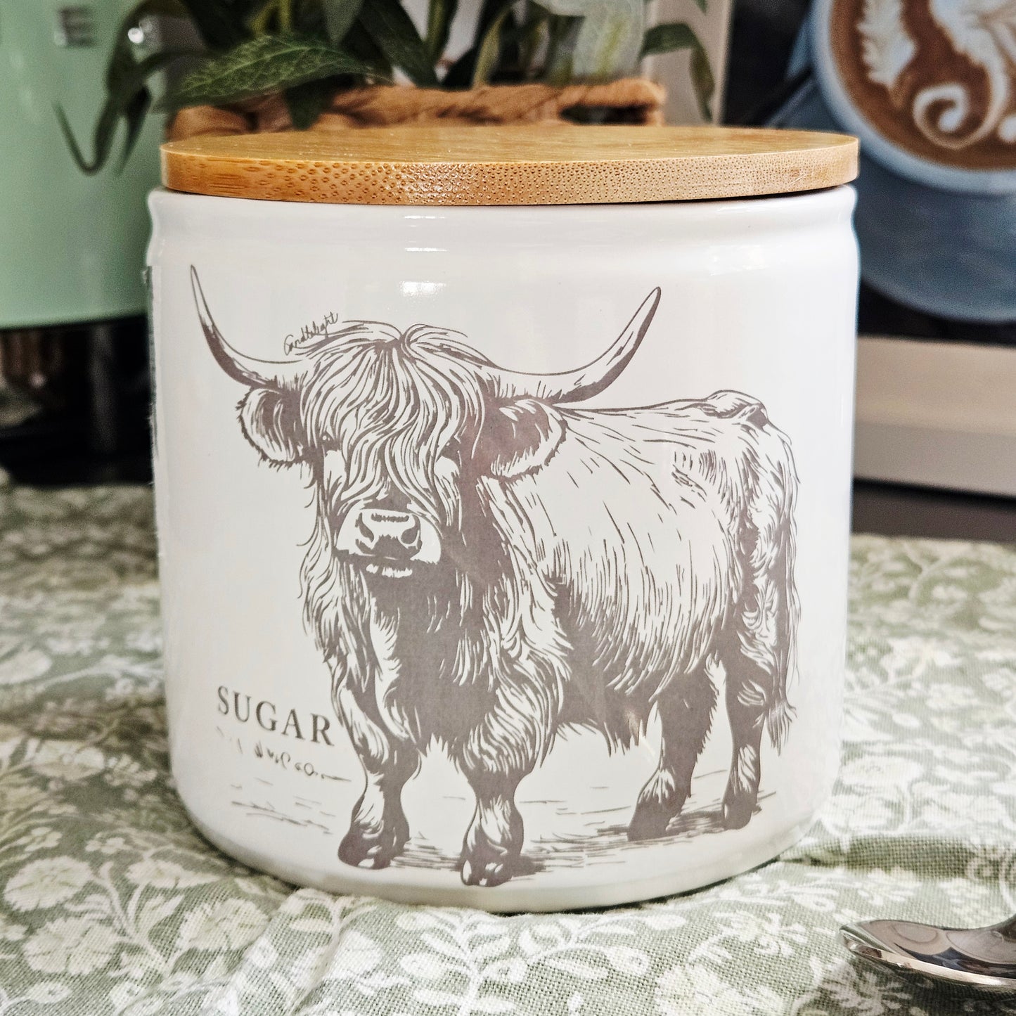White sugar canister with a highland cow design and wooden lid on 