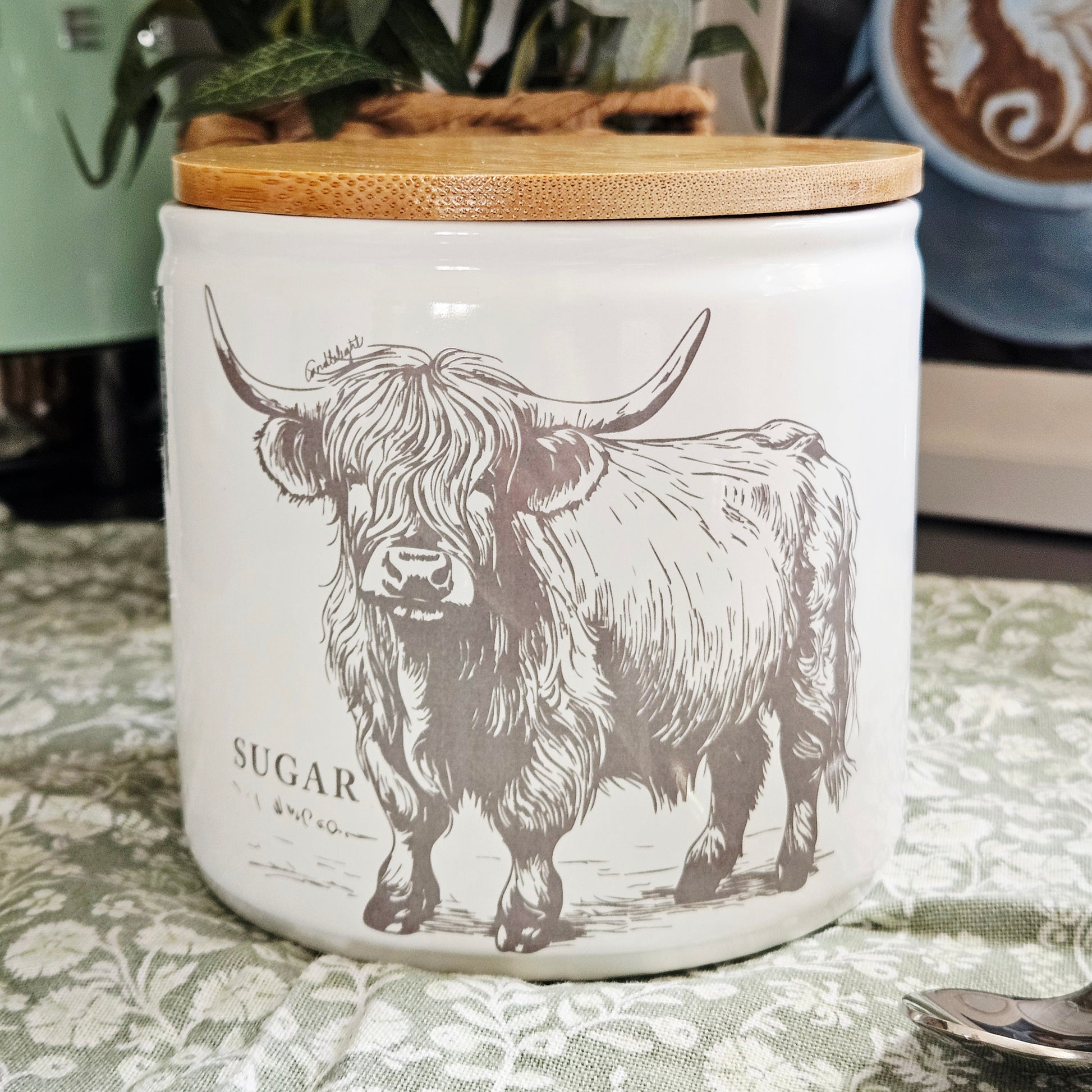 White sugar canister with a highland cow design and wooden lid on 