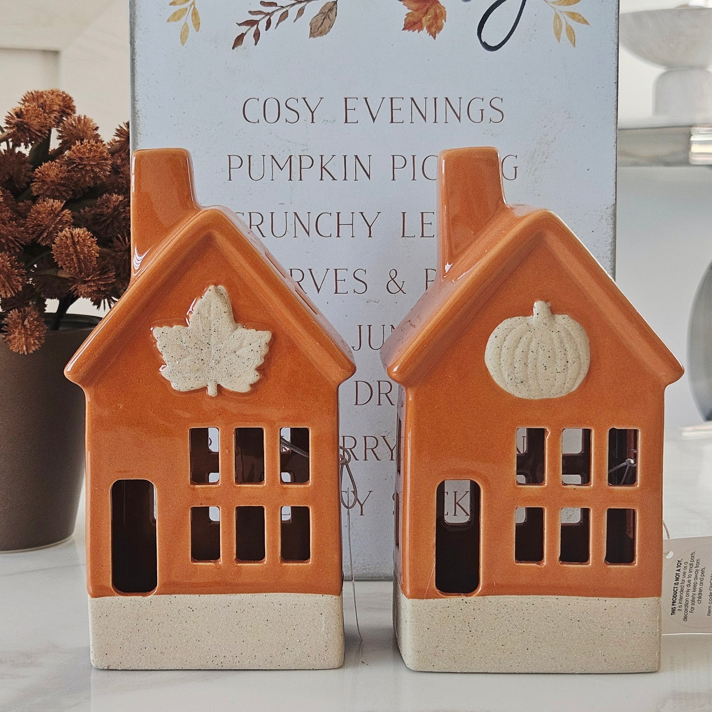 Two orange ceramic house-shaped led lanterns with pumpkin and leaf designs