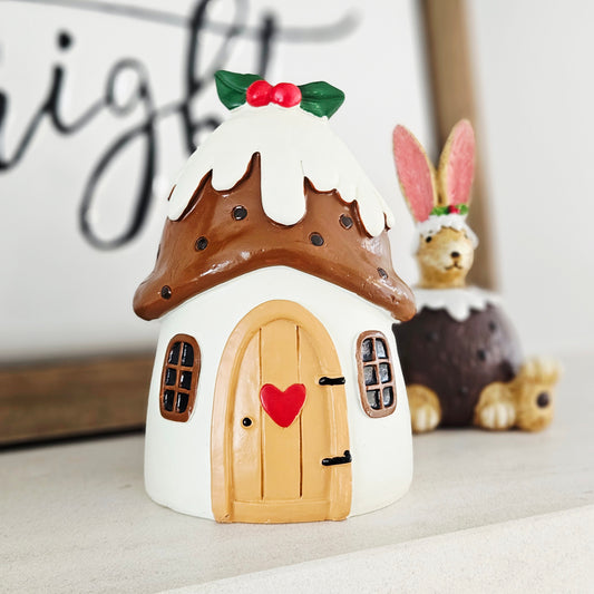 Decorative house-shaped christmas pudding with a heart door on a white surface.