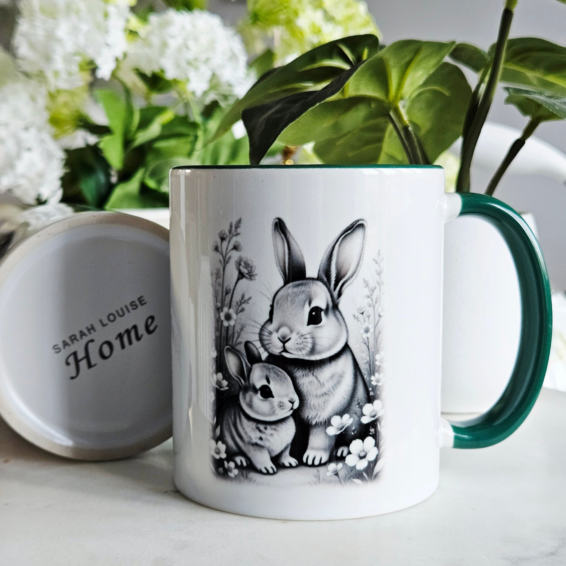 Mug with rabbit design and 'Sarah Louise Home' branding, surrounded by plants and flowers.
