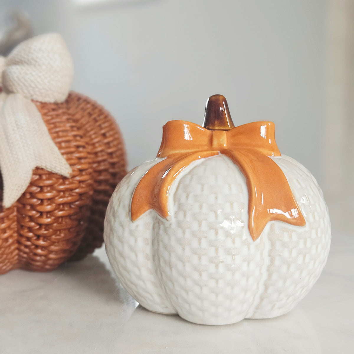 A white ceramic white check pumpkin-with a glossy orange bow and stem, 