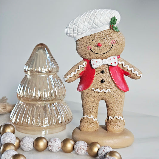 Decorative gingerbread man figurine with a glass Christmas tree and ornaments on a light background