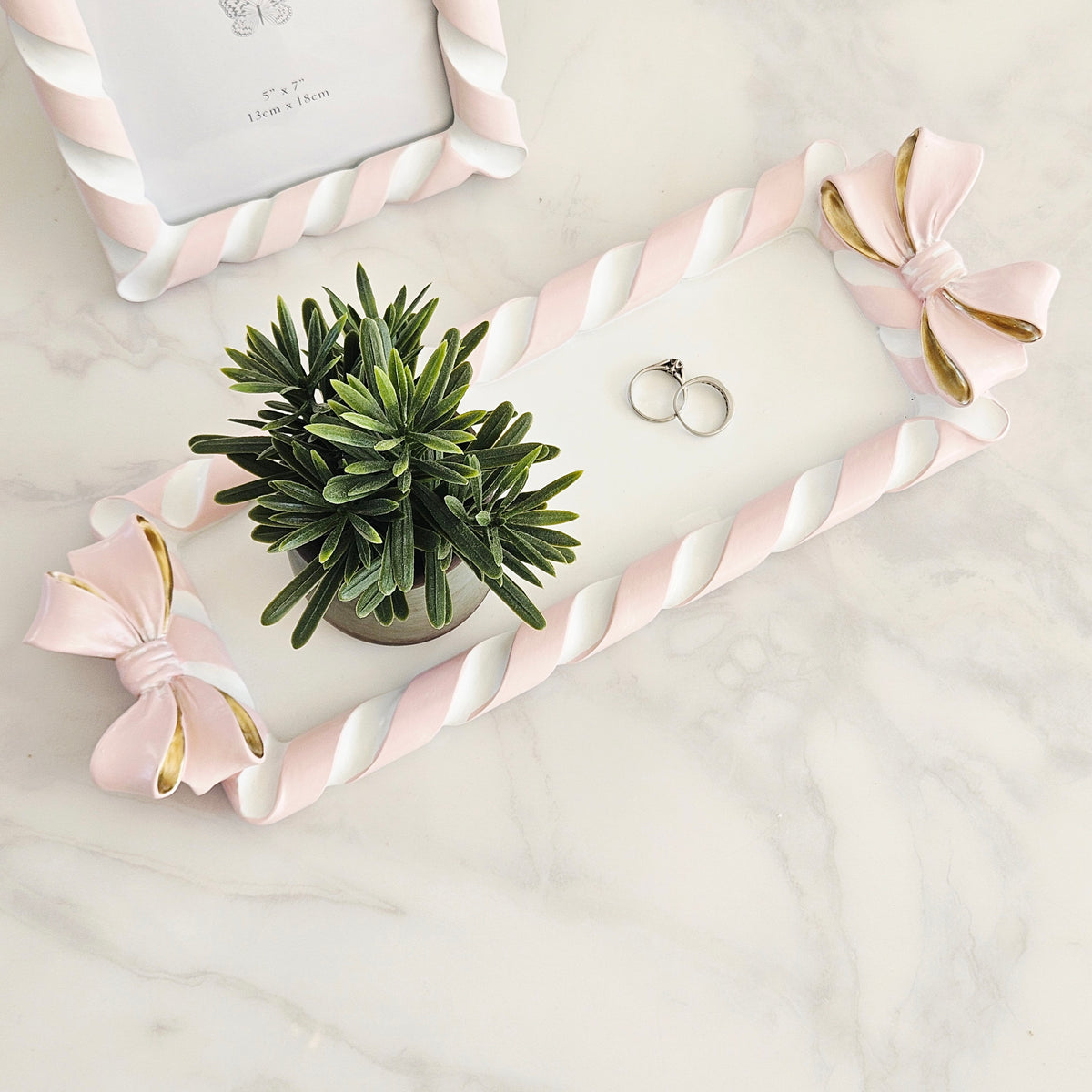 A decorative rectangular tray with a twisted rope border in pink and white, adorned with two large pink bows that have gold inner linings. 
