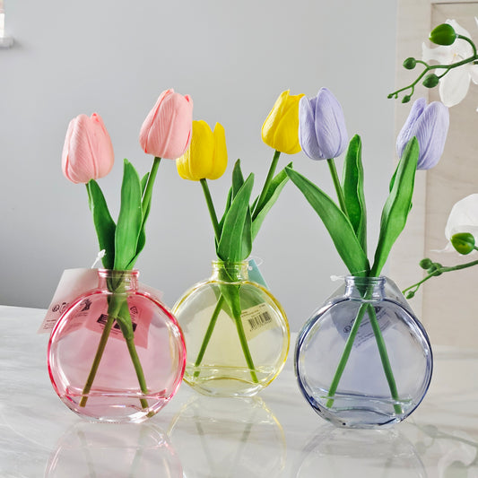 Three round glass vases with pink, yellow, and purple tulips and green leaves