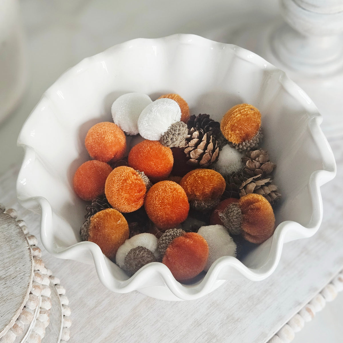 decorative fall elements, including orange pom-pom balls, white pom-pom balls, pinecones, and acorns,